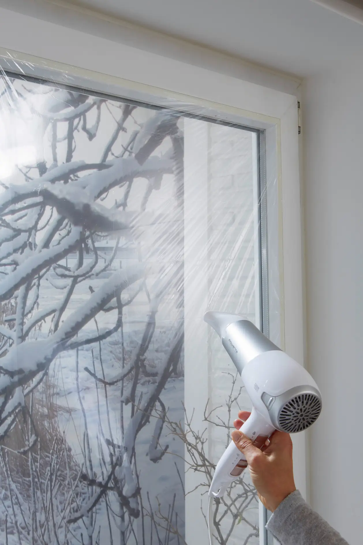 Föhn erhitzt Plastikfolie auf verschneitem Fenster