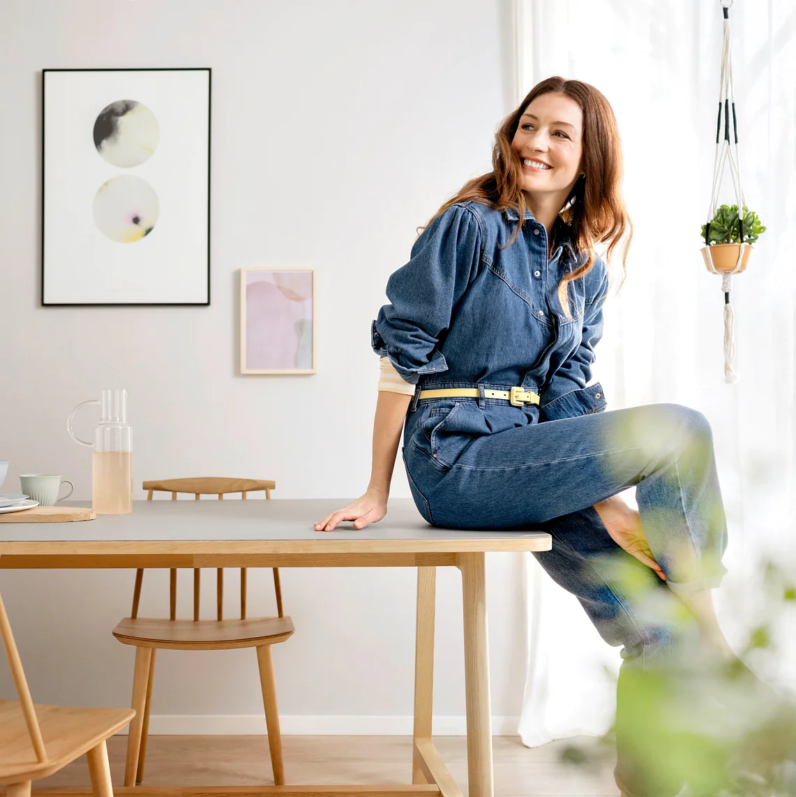 Wohnzimmer gestalten - Frau sitzt lachend auf der Kante eines Tisches, im Hintergrund Bilder