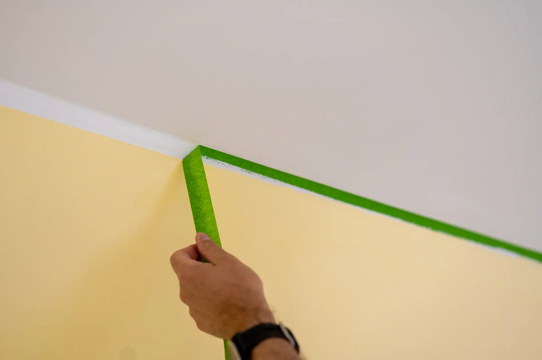 Painter removes masking tape and creates a sharp border between a yellow and white painted part of a wall. 