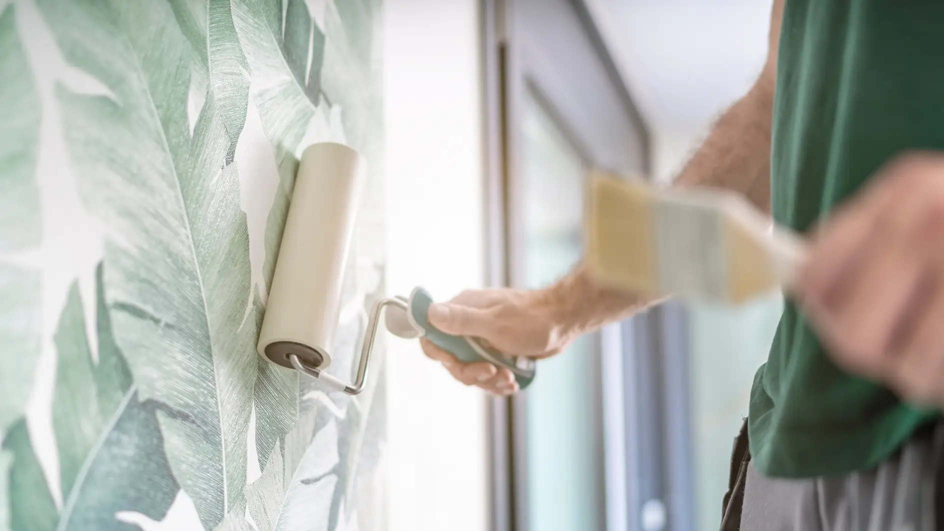 Maler drückt die frisch verklebte Mustertapete mit der Rolle an die Wand 