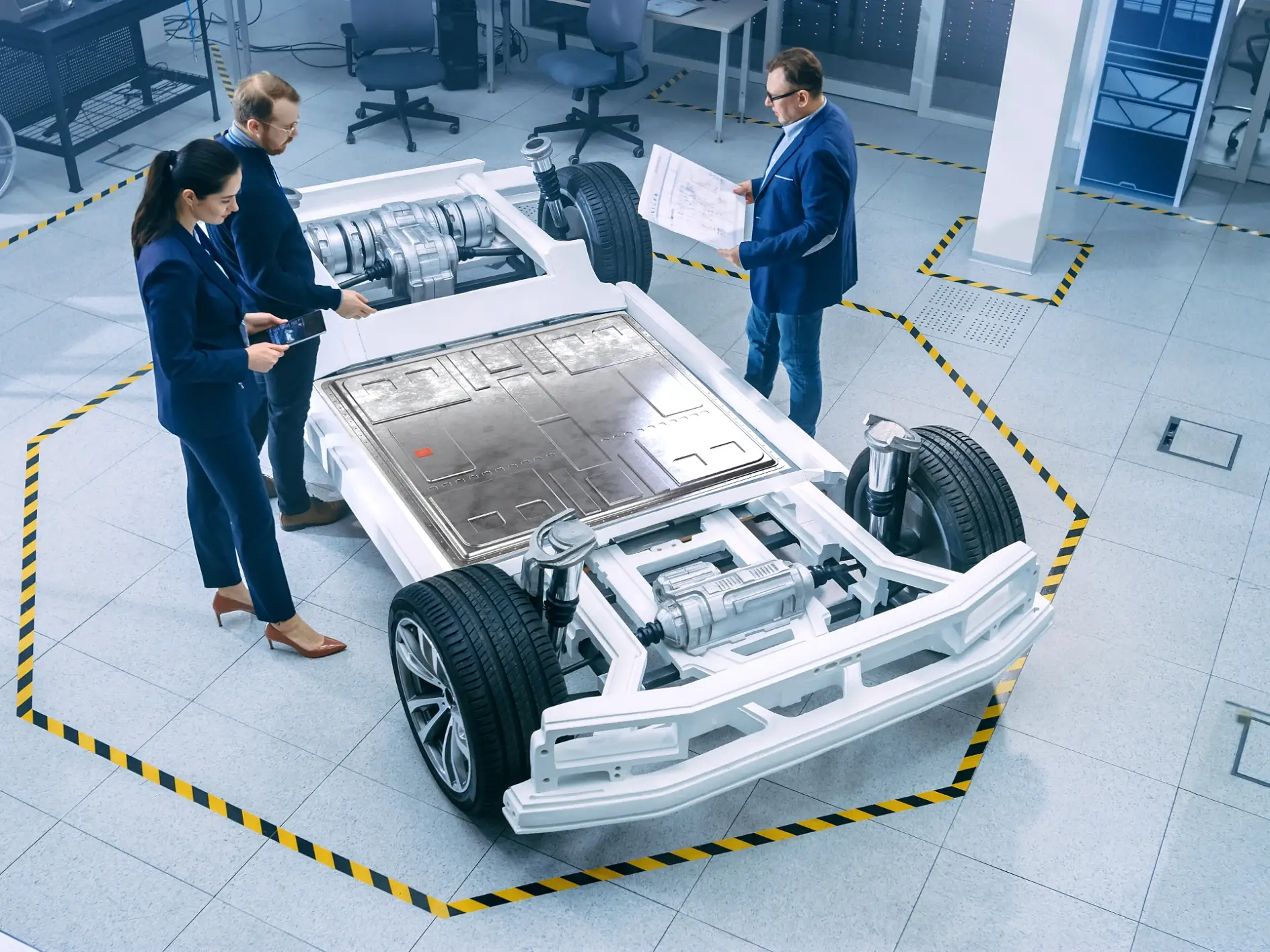 Automotive Design Engineers Talking while Working on Electric Car Chassis Prototype. In Innovation Laboratory Facility Concept Vehicle Frame Includes Wheels, Suspension, Engine and Battery.