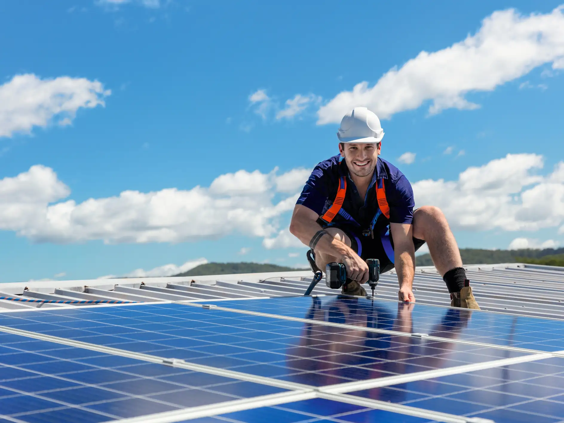 Técnico de paneles solares con taladro instalando paneles solares en el tejado en un día soleado