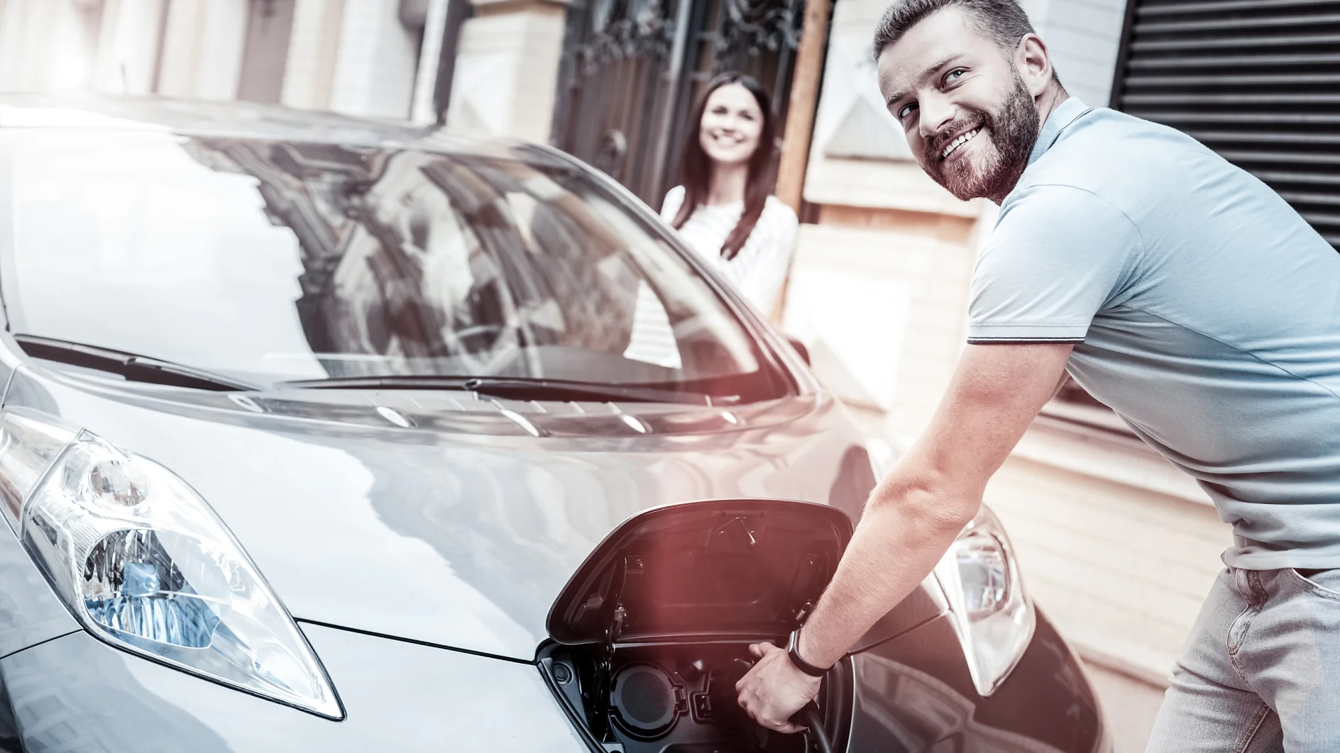 Transporte fácil y ecológico. Enfoque selectivo sobre un milenial feliz con una amplia sonrisa mientras sostiene una boquilla de carga y disfruta del proceso de suministro de energía al aire libre con su coche ecológico.